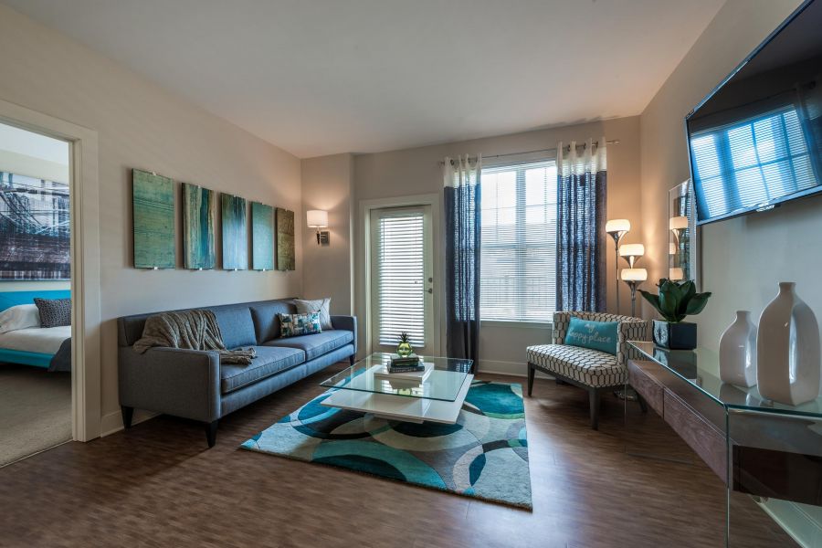 Pinnacle Apartments Modern living room with gray sofa, glass coffee table, accent chair, and large window with blue curtains.