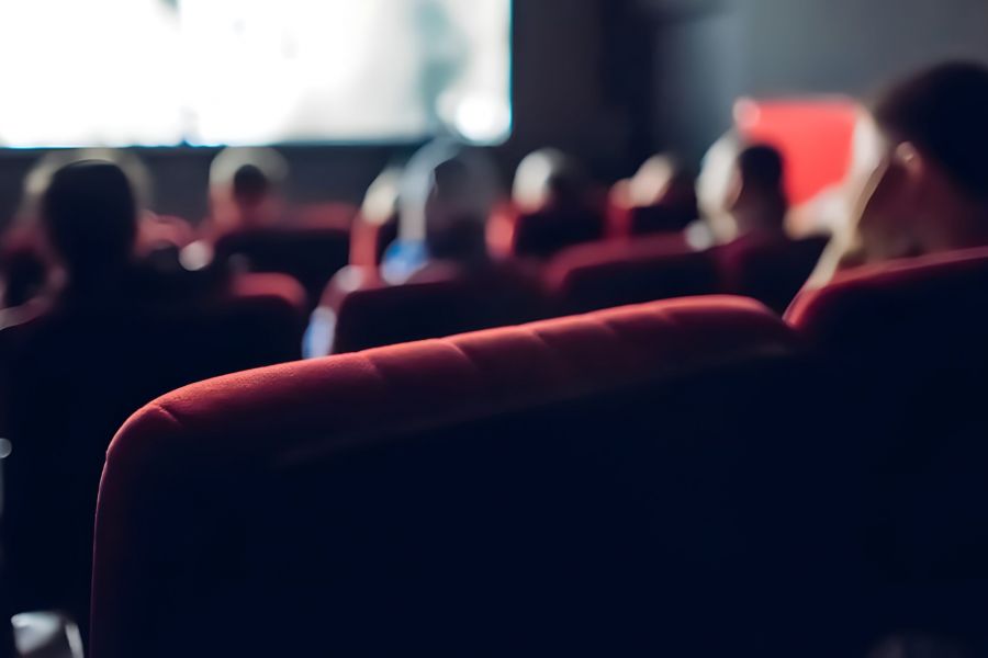 Pinnacle Apartments People sitting in red seats inside a dark movie theater, watching a film on a bright screen.