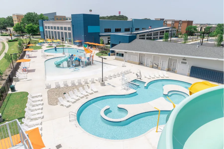 Pinnacle Apartments A modern outdoor aquatic center with pools, water slides, lounge chairs, and shaded areas on a sunny day.