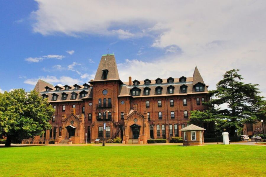 Pinnacle Apartments Historic brick building with tall, pointed roofs, set on a green lawn under a partly cloudy sky.