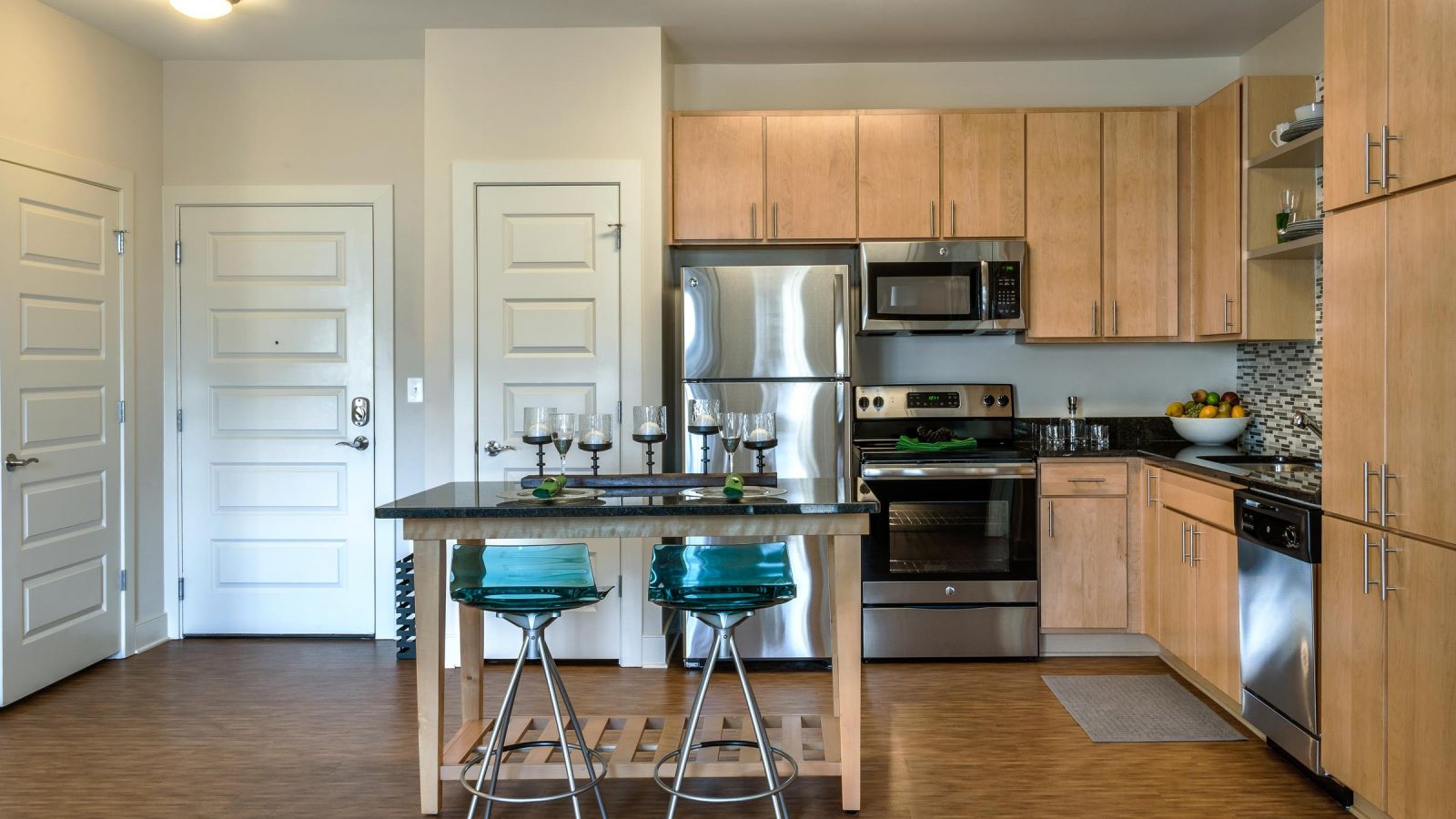 Modern kitchen and living area with white cabinets, stainless steel appliances, and a large island. Cozy seating area with a sofa and rug in the background. Bright and inviting atmosphere.