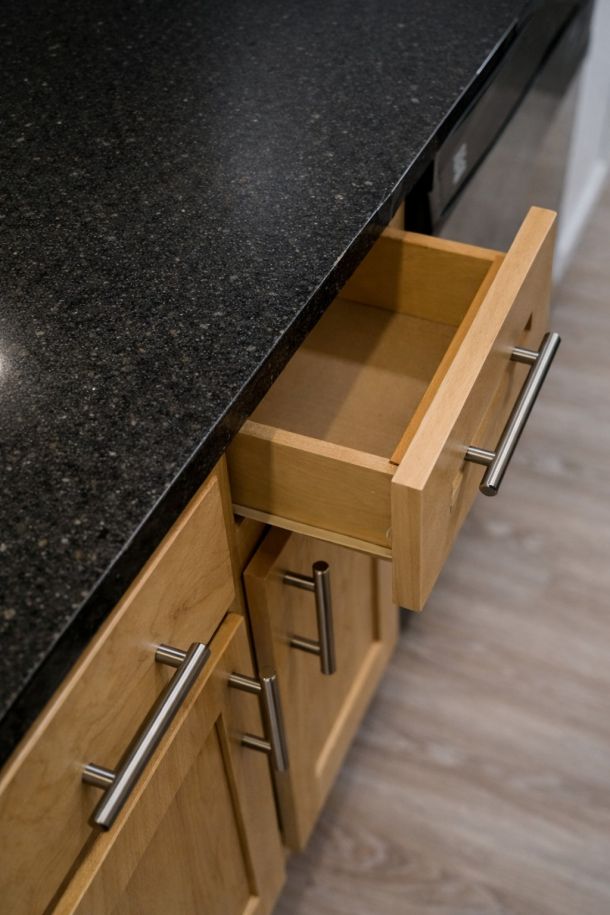 Pinnacle Apartment A wooden kitchen drawer is open under a black granite countertop.