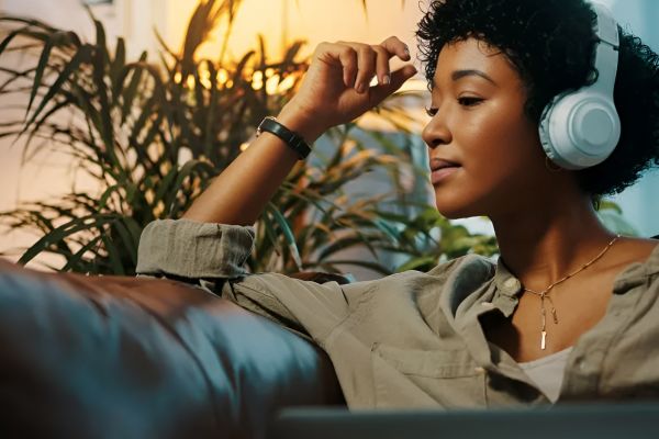 Attain on 5th apartment homes with Woman relaxing on a couch, wearing headphones, with plants and a lamp in the background.