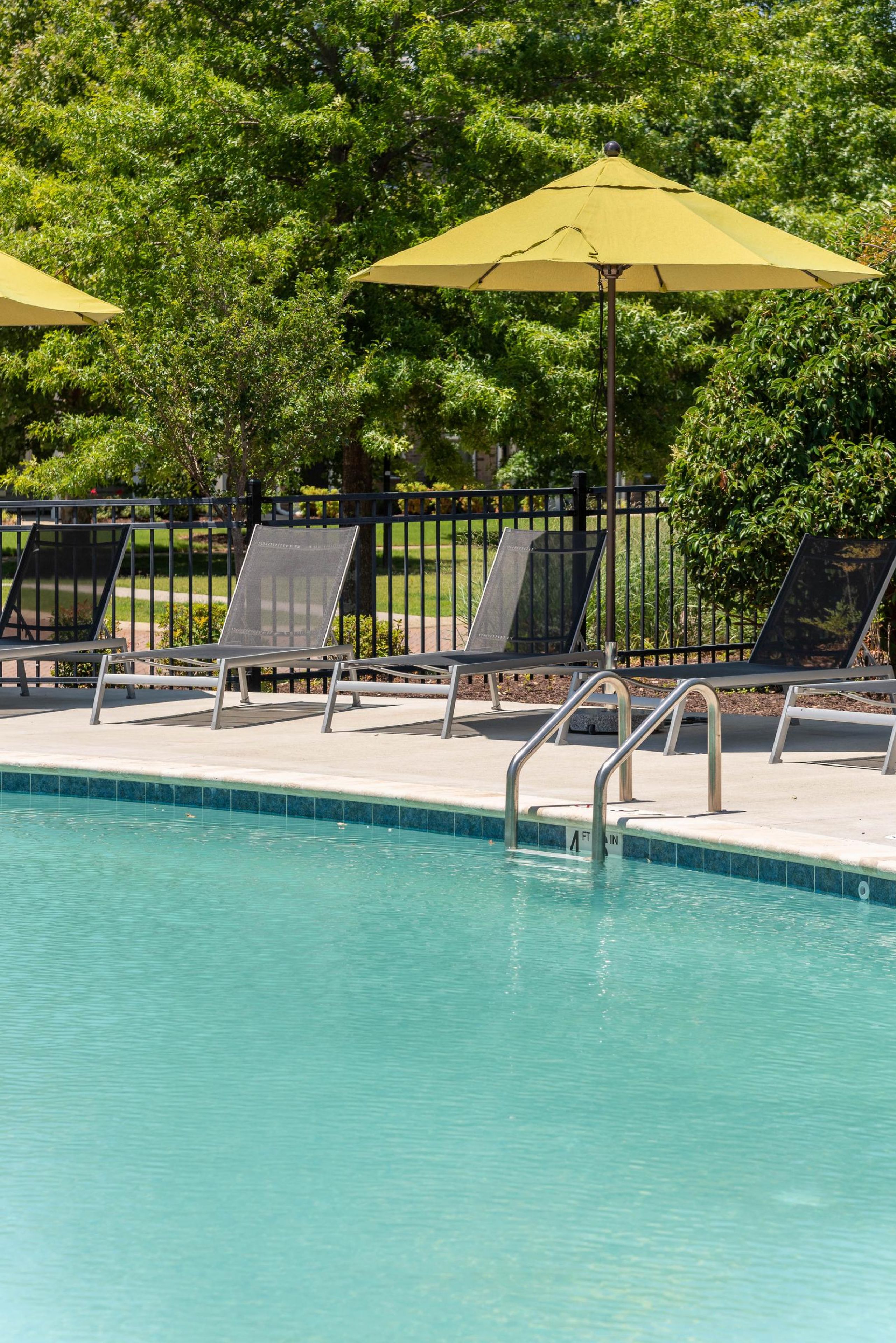 Pinnacle Apartments Four lounge chairs and two yellow umbrellas beside a clear outdoor swimming pool on a sunny day.