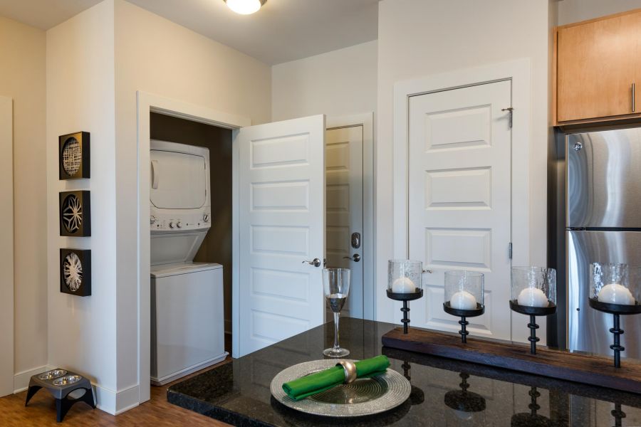 Pinnacle Apartments A stacked washer and dryer in a closet next to a kitchen with black countertops and decorative candles.