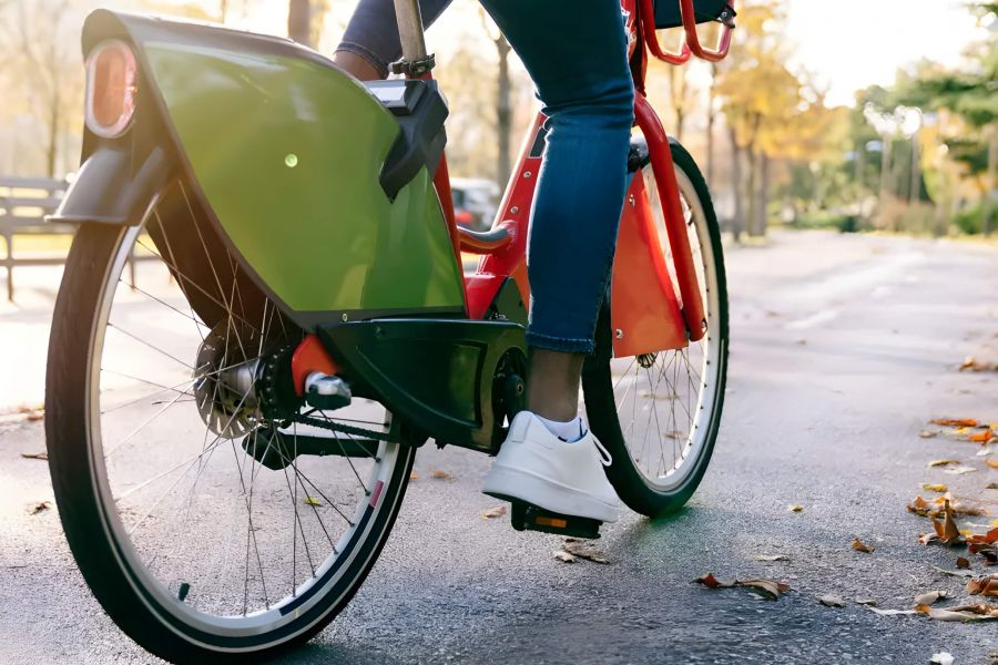 Pinnacle Apartments Person riding a red and green bicycle on a park path covered with autumn leaves.