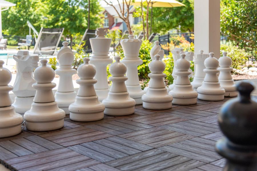 Pinnacle Apartments Large outdoor chess pieces on a tiled patio, with greenery and lounge chairs in the background.