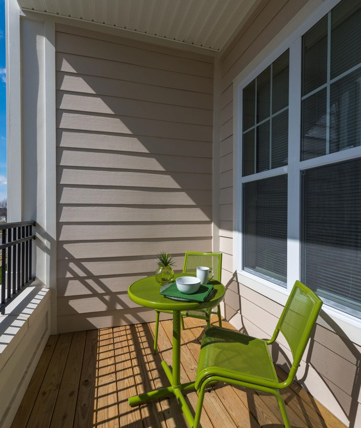 Pinnacle Apartments Green table and chairs on a sunny balcony with a teacup and small plant, next to a window.