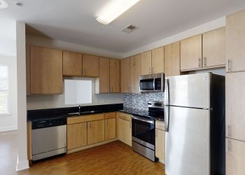 Pinnacle Apartments Modern kitchen with light wood cabinets, stainless steel appliances, and a gray tile backsplash.