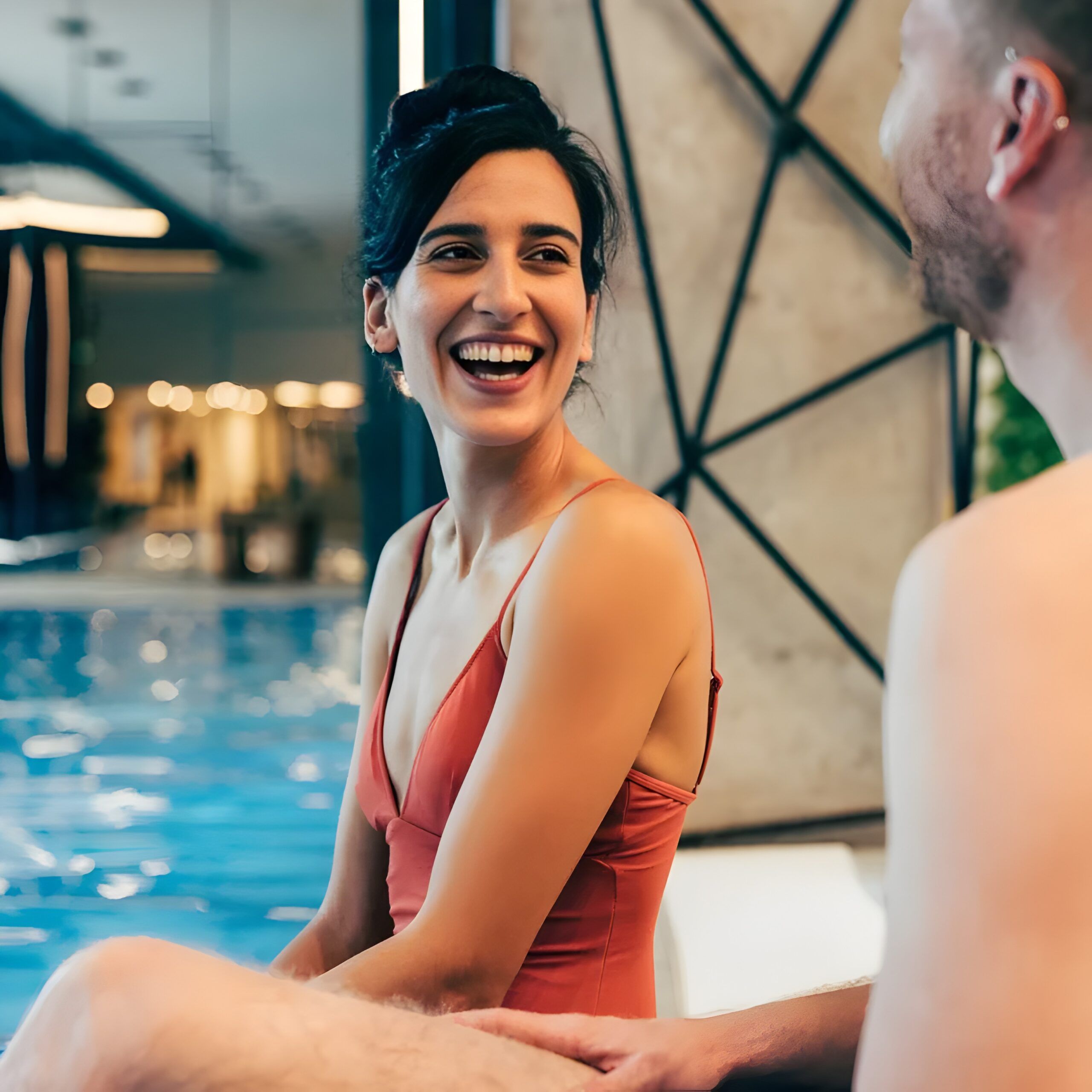 Pinnacle Apartments Woman in a red swimsuit smiling and talking with a man by an indoor pool.