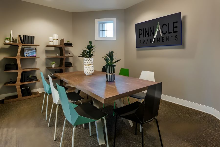 Pinnacle Apartments Modern meeting room with a wooden table, mixed chairs, plants, and a Pinnacle Apartments sign on the wall.