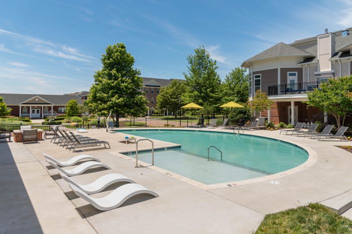 Pinnacle Outdoor swimming pool with lounge chairs, umbrellas, and surrounding apartment buildings on a sunny day.