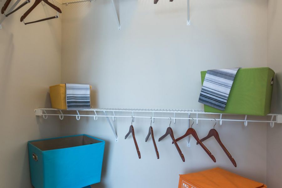 Pinnacle Apartments Walk-in closet with empty hangers, baskets, a suitcase, and a couple of decorative pillows on shelves.
