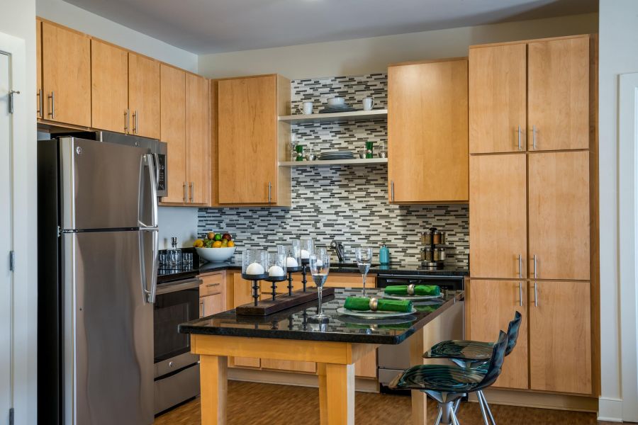Pinnacle Apartments Modern kitchen with wood cabinets, stainless steel appliances, and a black countertop island with bar stools.
