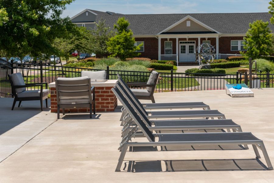 Pinnacle apartment homes with Several lounge chairs and outdoor seating are arranged on a patio near a fire pit, with a building in the background.