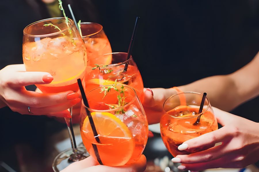 Pinnacle Apartments People clinking glasses of orange cocktails with ice, garnished with orange slices and herbs.