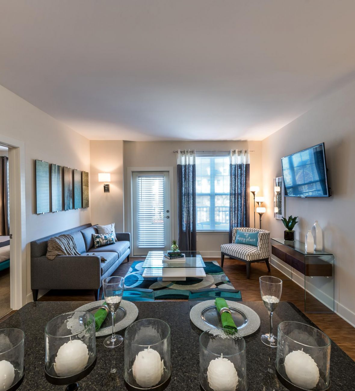 Pinnacle Apartments Modern apartment living room with a gray sofa, wall-mounted TV, and a dining table set for four.