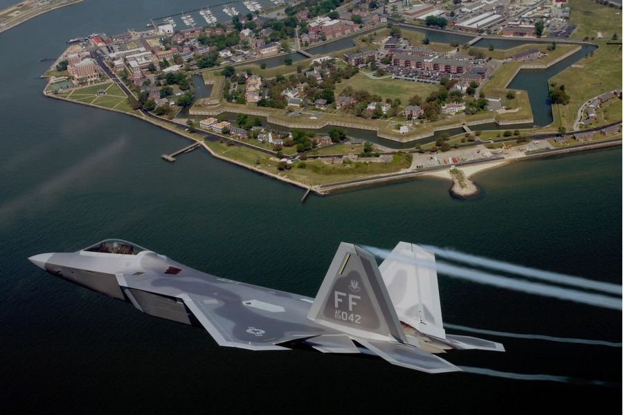Pinnacle apartment homes with A fighter jet flies over a coastal fort with a marina and buildings in the background.
